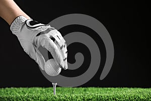 Player putting golf ball on tee against black background. Space for text