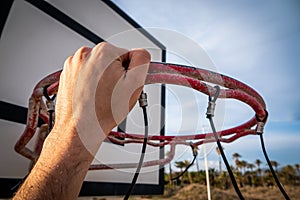 Player's hand holding the basketball hoop on the beach under a cloudy sky