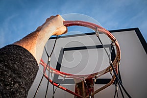 Player's hand holding the basketball hoop on the beach under a cloudy sky