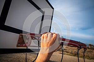 Player's hand holding the basketball hoop on the beach under a cloudy sky