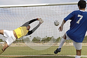 Player Scoring Goal While Goalkeeper Diving To Save It