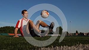 Player sitting on the grass and bouncing a soccer ball with feet