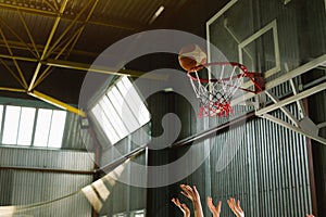 Players hands and ball through basketball hoop. Indoor shot, sport gym, championnat, window sunny light.