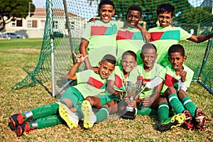Players win games, teams win championships. Portrait of a boys soccer team posing with their trophy on a sports field.