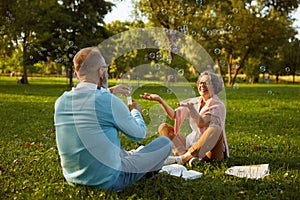 Playful senior couple blowing soap bubbles while rest in park