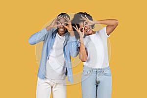 Playful African American couple making funny faces with fingers imitating glasses