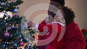 Playful African American father and little son enjoying Christmas eve at home indoors. Side view portrait of carefree