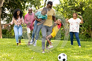 Playful african american multi-generational family playing soccer together in backyard on weekend photo