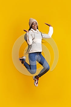 Playful african winter girl having fun over yellow studio background