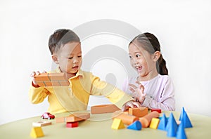 Playful asian little girl and baby boy playing a colorful wood block toy on table over white background. Sister and her brother