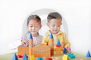 Playful asian little girl and baby boy playing a colorful wood block toy on table over white background. Sister and her brother