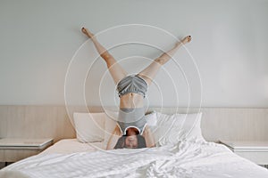 Playful woman is doing upside down pose on the bed.