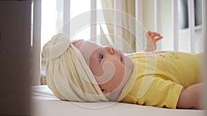 Playful baby girl in yellow clothes lies in bassinet closeup