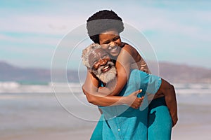 Playful bearded african american senior man piggybacking happy mature woman against sea and sky