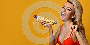 Playful beautiful woman having fun eating delicious hot dog smiling and looking at camera.