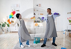 Playful black couple having mock fight with mop and detergent, being silly during house cleanup, indoors