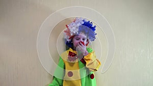 A playful  boy in a clown costume in a wig puts on a false nose and then throws it jokingly.