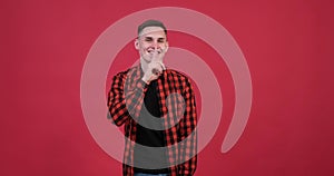 Playful caucasian man showing shh gesture on red background