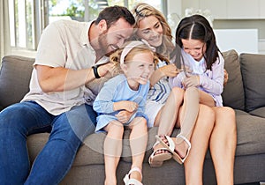 Playful caucasian parents tickling their children while relaxing together on a sofa at home. Carefree little girls