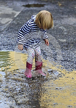 Playful child jump into puddle in boot after rain