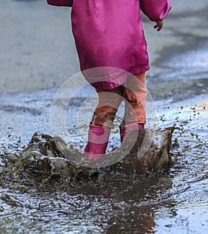 Playful child jump into puddle in boot after rain