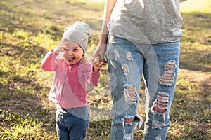 Playful child with mother walking together with holding hands in summer park on grass. Main subject is child. Unrecognizable mothe