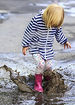 Playful child outdoor jump into puddle in boot