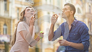 Playful couple blowing soap bubbles, enjoying time together, summer date