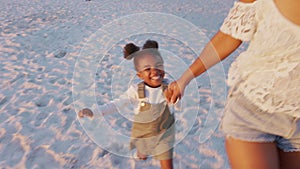 Playful cute little daughter running on beach with young black mother