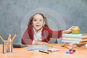 A playful cute little girl is having fun while relying on thick books on a gray background. Her hair is made in