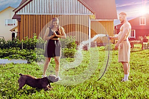 Playful dog grabs splashes of water from garden hose with its mouth during an evening walk in courtyard of country house