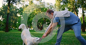Playful dog hold leash in teeth playing. Smiling man pulling rope in park.