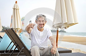 playful elderly man sitting on beach chair,smiling and pointing to camera