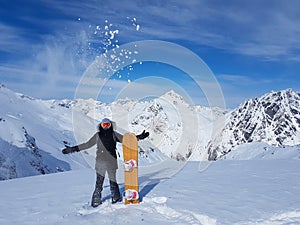 Playful female snowboarder throws a handful of fresh snow high in the air.