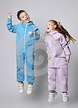 Playful frolic kids boy and girl in blue and pink jumpsuits are jumping together, having fun, laughing loudly