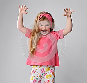 Playful, frolic redhead kid girl in pink t-shirt and colorful pants plays beast holding hands with claws up