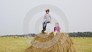 Playful girl and boy jumping on haystack at harvesting field in village. Happy teenagers jumping on haystack on