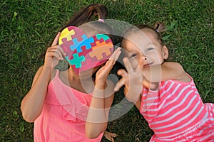 A playful girl next to sister hiding behind a heart with puzzles