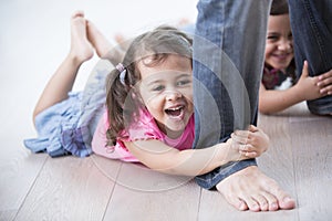 Playful girls holding father's legs on hardwood floor