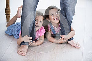 Playful girls holding father's legs on hardwood floor