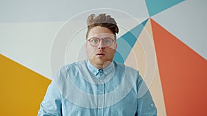 Playful guy putting on glasses then looking at camera shocked on colorful background