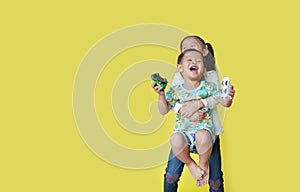 Playful of happy asian sister hugging and lift up her little brother standing on yellow background with copy space