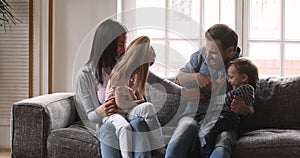 Playful happy parents and small children playing tickling on sofa