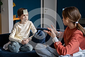 Playful interested diverse pensive children boy and girl with stickers on forehead guessing Who Am I