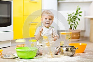 Playful kid boy with face in flour surrounded kitchenware and foodstuffs photo