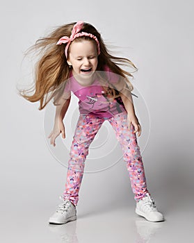 Playful kid girl in summer clothes colorful pant and pink t-shirt laughs loudly with her eyes closed shakes her head