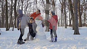 Playful kids high-fiving with each other near snowman in winter park