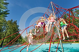 Playful kids sit on red ropes of playground