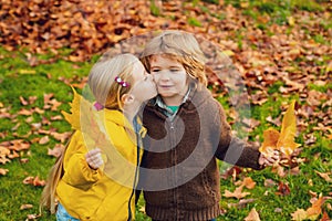 Playful little cute couple boy and girl walk on autumn park, have fun, kiss, enjoy good sunny day.