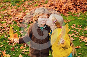 Playful little cute couple boy and girl walk on autumn park, have fun, kiss, enjoy good sunny day.